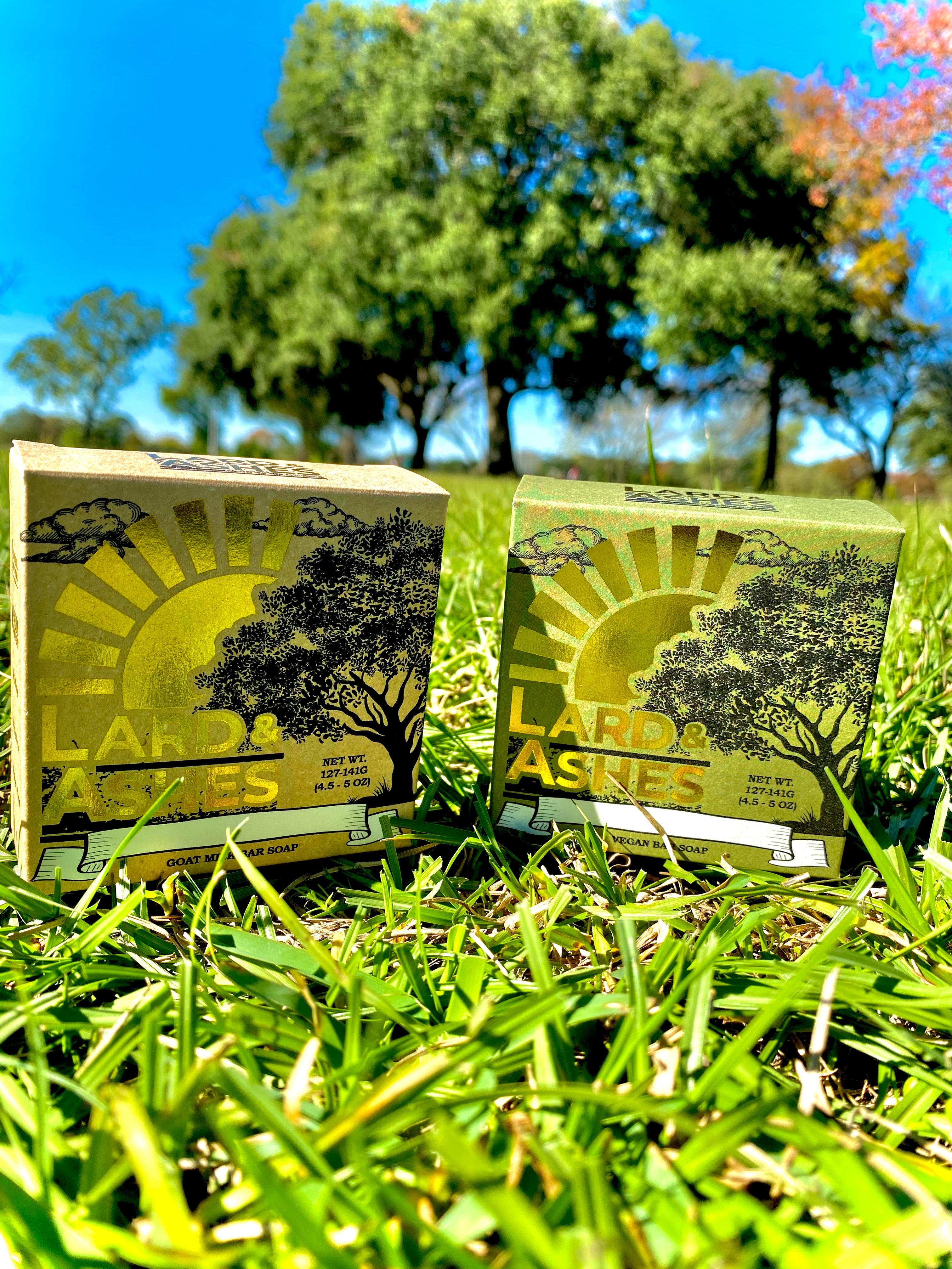 A couple of Lard and Ashes Soap Boxes on top of a lush green field